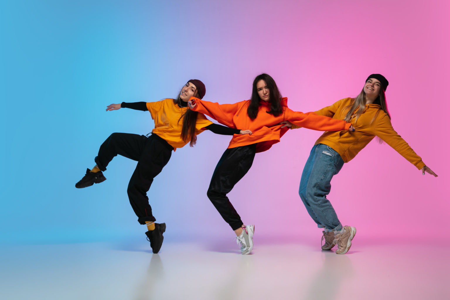 Beautiful sportive girls dancing hip-hop in stylish clothes on colorful gradient studio background in neon light. Youth culture, movement, style and fashion, action. Fashionable bright portrait.